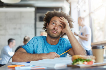 Knowledge and education. Unhappy Afro American university student wearing blue t-shirt looking up...
