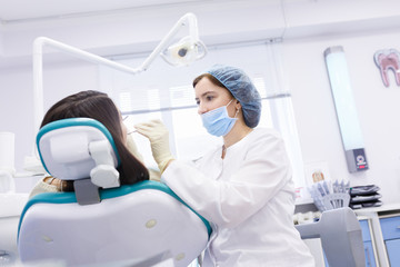 Young female patient in dentist office. Dentist examines the patient teeth at dental chair with open mouth, dental procedure in clinic