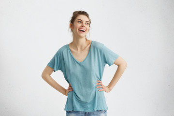 Isolated portrait of attractive cheerful young European woman wearing oversize blue top smiling broadly, feeling happy and carefree while having fun indoors, looking away with pleasure and joy