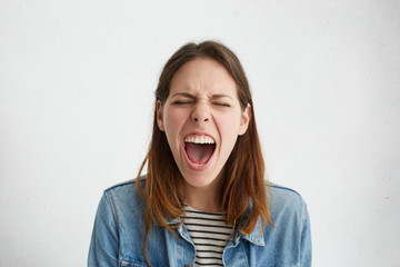Studio shot of emotional stressed female dressed in trendy clothing shouting in fury and rage,...