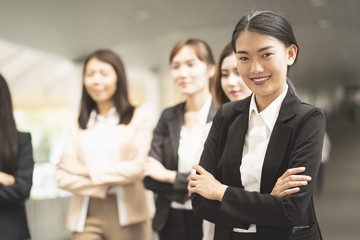 Portrait of cheerful businesswoman with arms folded standing in front of colleagues