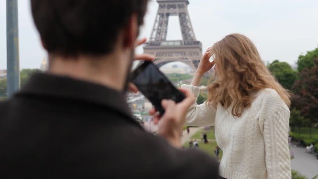 couple of tourists in Paris, man taking mobile phone photo of his girlfriend with Eiffel tower