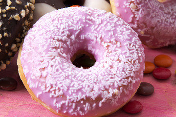 Assortment of colorful donuts with candies on pink wooden background