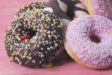 Assortment of colorful donuts with candies on pink wooden background
