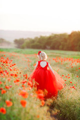 countryside, childhood, holidays, summer concept - small fair-haired fairy in beautiful scarlet poofy dress with tulle skirt rushing through the field of poppies