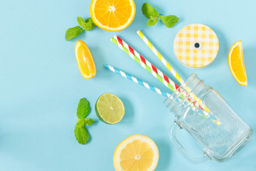 Empty mason jar on blue background, top view. colorful paper straws and fruits around.