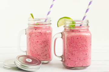 Smoothies with raspberries and strawberries served in mason jars with colorful paper straws, white background.