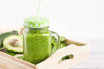 Green smoothie with vegetables served in colorful mason jar with paper straw on wooden tray.