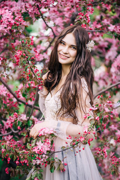 beautiful cute brunette girl bride in boudoir lace transparent dress smile near the tree blossoms with pink flowers
