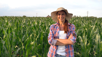Beautiful girl (woman) farmer smiling, looking, checking corn fields, straw hat, greens background. Concept: ecology, corn, bio product, inspection, water, natural products, professional, environment.