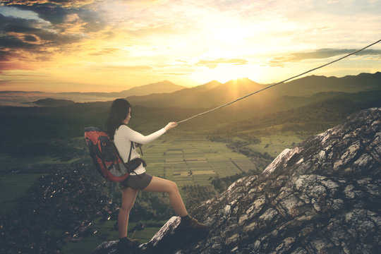 Asian female hiker climbing a steep mountain © Creativa Images