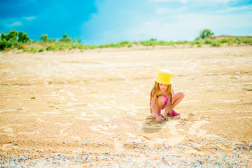Little girl with long hair playing with sand on shore of beach sea on sunny day. Selective focus