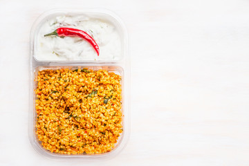 Couscous salad with yogurt dip in lunch box on white wooden background , top view