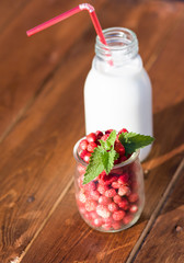 Wild strawberies and mint against bottle of milk outdoor. Focus on berries
