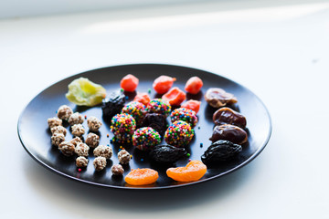 a set of nuts, sesame seed candy dried apricots dates raisins candied fruit in a black bowl on a white background close-up