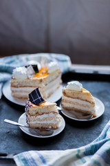 a beautiful delicious cake and the pieces in three white saucers beige yellow on cutting Board on dark black background close-up