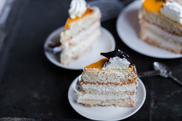 a beautiful delicious cake and the pieces in three white saucers beige yellow on cutting Board on dark black background close-up