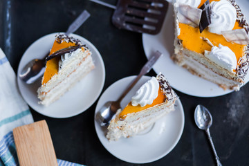 a beautiful delicious cake and the pieces in three white saucers beige yellow on cutting Board on dark black background close-up