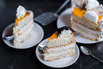 a beautiful delicious cake and the pieces in three white saucers beige yellow on cutting Board on dark black background close-up