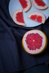 half cut grapefruit and pieces of fruits in a white plate on the kitchen towels cloth rags blue grey dark hue close-up of copyspace