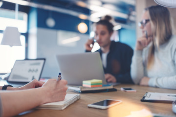 Business team brainstorming in coworking office. Laptop and paperwork on the wooden desk. Three people. Intentional lens flares