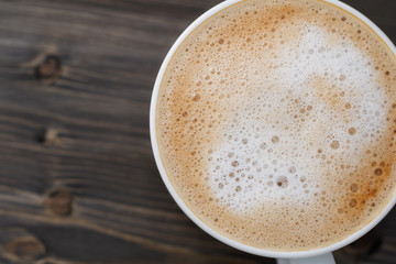 Top view of a white cup of cappuccino on a wooden black table. Close-up, macro shot. Copy space.