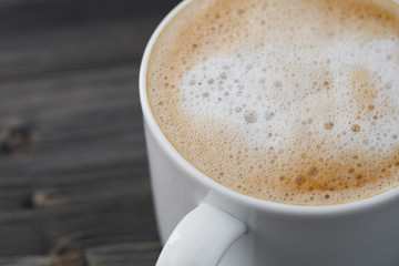 Close-up of a white cup of cappuccino on a wooden black table. Macro shot.