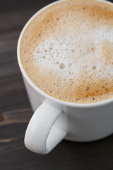 Close-up of a white cup of cappuccino on a wooden black table. Macro shot.