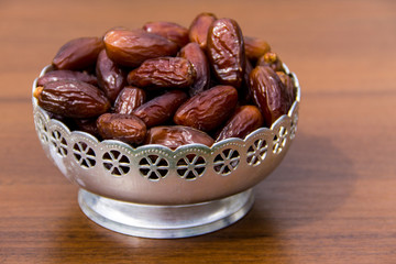 Dates fruit on a silver bowl on wooden table. The Muslim feast of the holy month of Ramadan Kareem