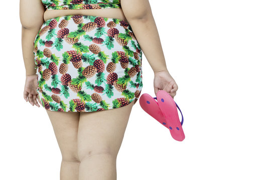 Overweight woman in bikini holds sandals