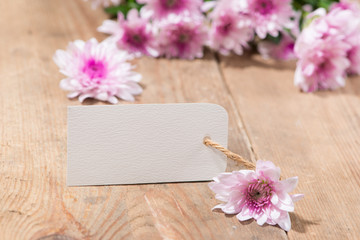 Blank white tag paper with color flowers on wooden background. Top view. Mock up