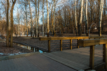 Central park (Dinamo park) in Voronezh, Russia. Spring park in the morning, a creek between the trees, wooden bridge over the stream and remainder of the snow on the ground.