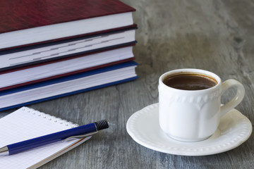 A white cup of coffee, notebooks  and pen.