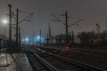 Fototapeta na wymiar Plehanovskaya station in Voronezh, Russia. Railway station in the night, bad weather, rails and wires under the cloudy sky. Red railway signals between the rails.