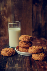 A close-up of a stack of pumpkin oat cookies on white parchment and gold swirl paper with golden raisins, cacao nibs and a glass of almond milk in the background.