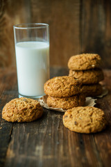 A close-up of a stack of pumpkin oat cookies on white parchment and gold swirl paper with golden raisins, cacao nibs and a glass of almond milk in the background.
