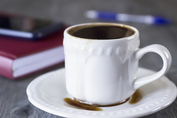 A white cup of coffee, notebooks  and pen.