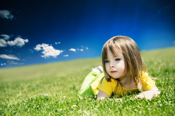 Fototapeta na wymiar A little girl lies on a green lawn on a warm summer day.