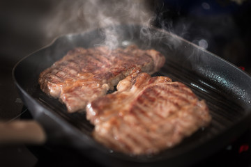 Beef steak fry in a frying pan in smoke and steam