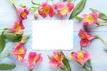 Pink alstroemeria flowers with sheet of paper on blue wooden table