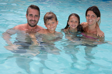 family of four are 4 in swimming pool summer in water