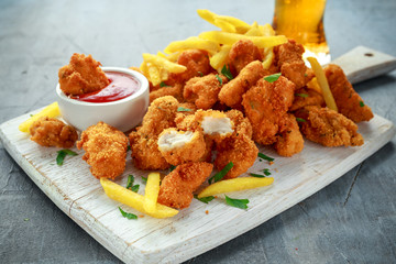 Fried crispy chicken nuggets with french fries, ketchup and beer on white board