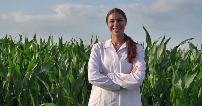 A plant specialist, examines the corn fields, in a white robe, the girl (woman) smiles, the background is green. Concept: ecology, bio product, inspection, water, natural products, professional, green