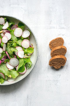 Healthy spring salad with radish and lettuce mix. Sliced homemade bread with seed. White background. Vertical photo