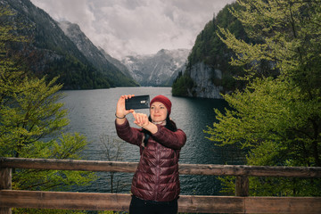 Fototapeta na wymiar Germany. Berchtesgaden National Park. The girl makes selfie on a viewing platform with a view of the lake Konigssee