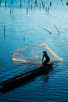 Silhouette of Fisherman catching fish in lake by using fishing net at beautiful sunset time.