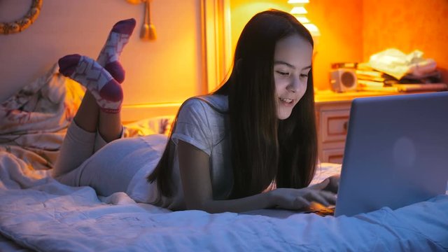 Beautiful girl lying on bed at night and using her laptop