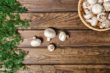 Mushrooms in the basket and dill on a wooden table, the top view. A still life with mushrooms.