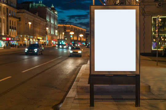 Vertical Blank Glowing Billboard On Night City Street. In Background Buildings And Road With Cars. Mock Up.