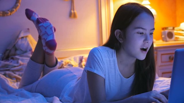 4k footage of teenage girl lying on bed and having conversation through internet on laptop